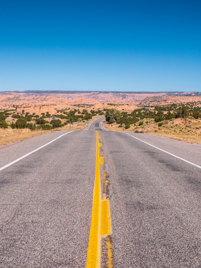 Open New Mexico desert highway stretching toward distant mesas under a wide sky